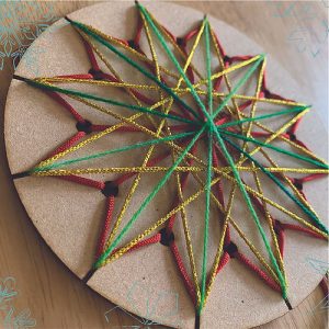 Wooden circular template showing lacing of a snowflake pattern with different coloured yarn.